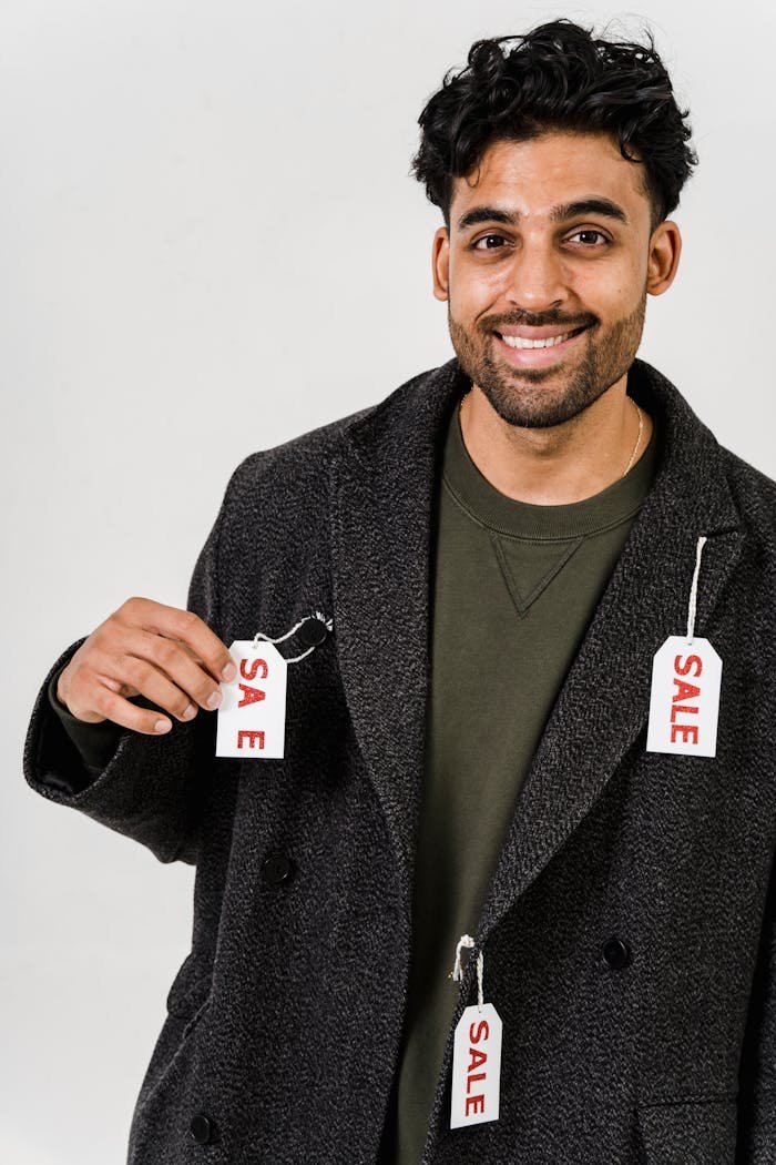 A man wearing a coat adorned with sale tags, smiling, representing discounts.